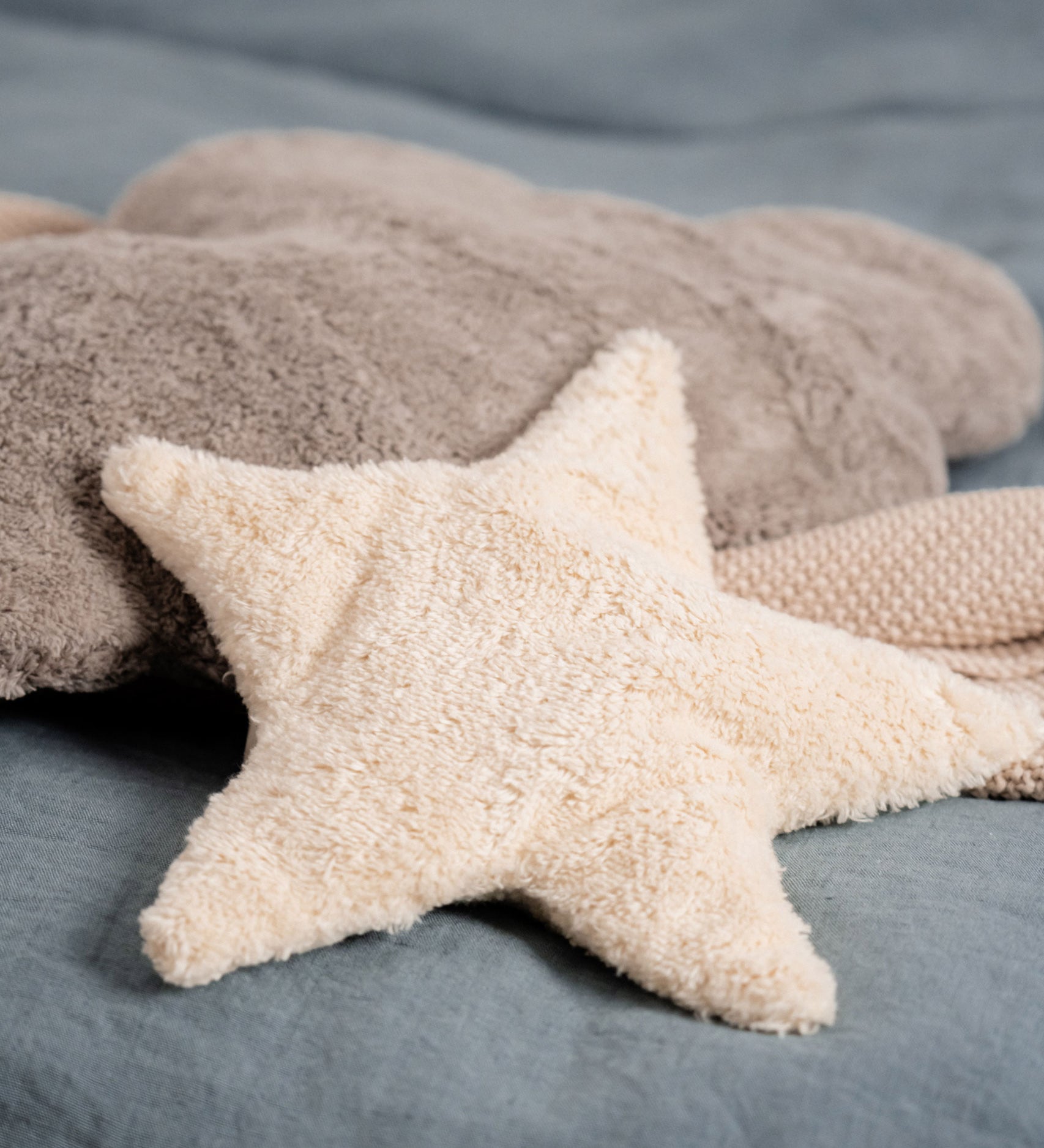 A light yellow, star shaped warming cushion from Senger placed on a  bed with a grey cloud cushion.