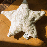 A  Senger light yellow coloured star shaped warming cushion placed on a wooden surface.