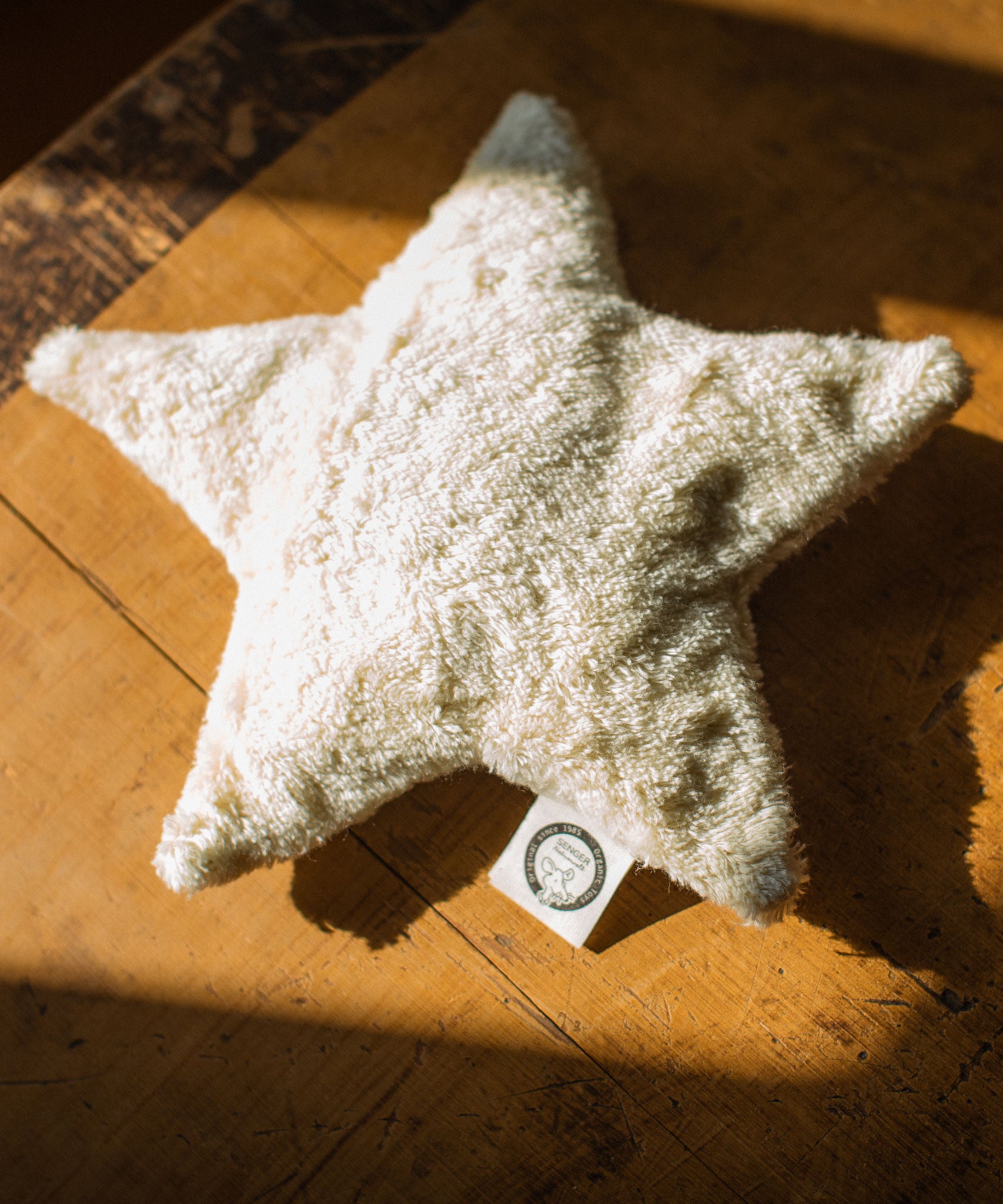 A  Senger light yellow coloured star shaped warming cushion placed on a wooden surface.