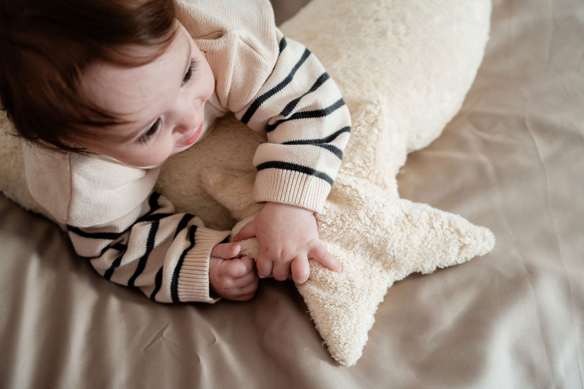 A young child laying besides a Senger light yellow, star shaped warming cushion.