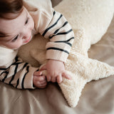 A young child laying besides a Senger light yellow, star shaped warming cushion.