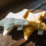 Two Senger star shaped warming cushions placed on the top of a trunk. One is a light yellow, off white colour and the other is a bright yellow colour.