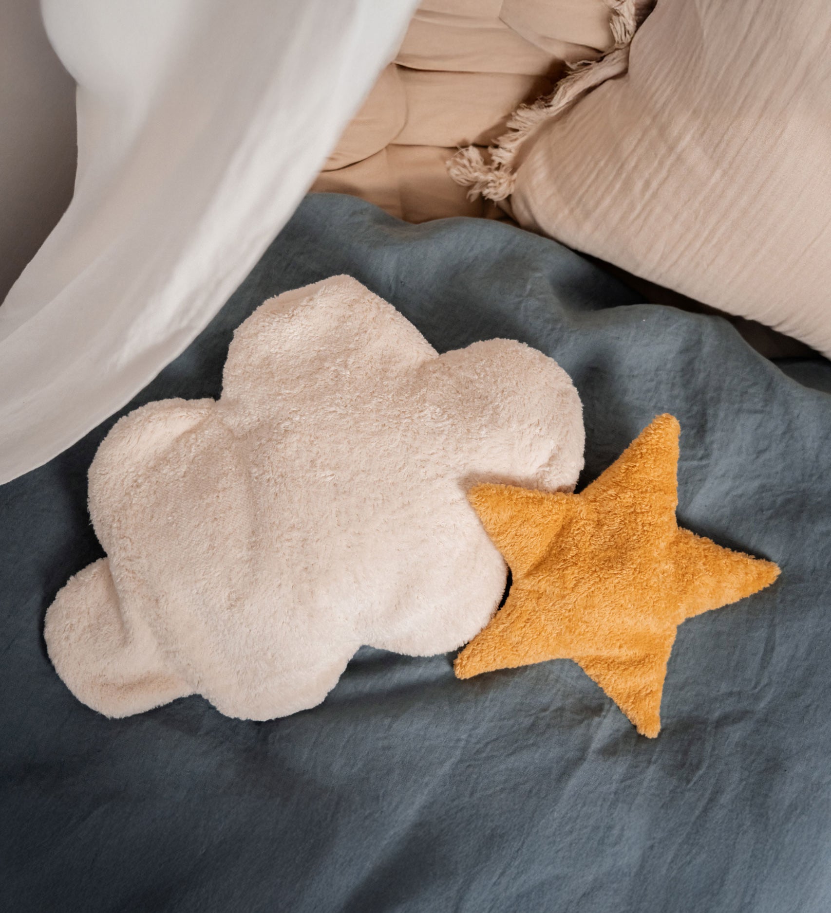 A yellow Senger star shaped warming cushion placed on a bed next to a white cloud cushion.