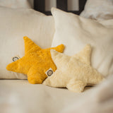 Two Senger star shaped warming cushions placed on a bed. One is a light yellow, off white colour and the other is a bright yellow colour.