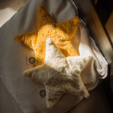 Two Senger star shaped warming cushions placed on a bed. One is a light yellow, off white colour and the other is a bright yellow colour.