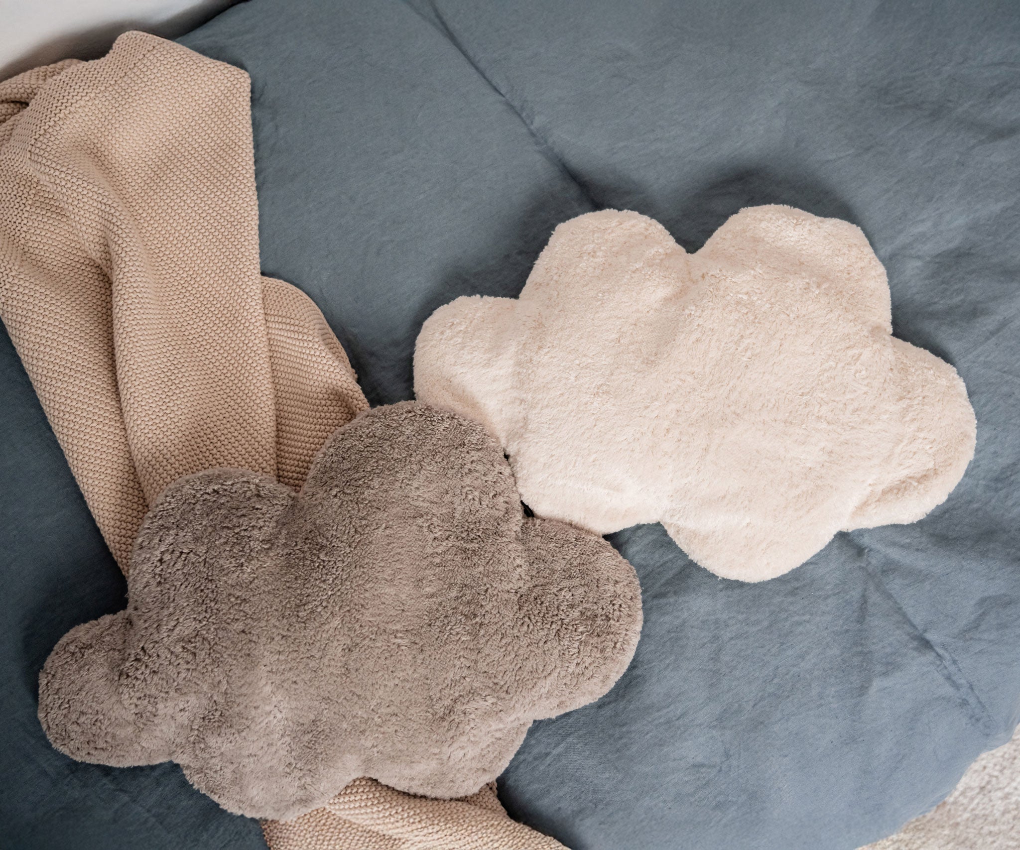 A white and grey cloud shaped Senger warming cushions placed on a bed.