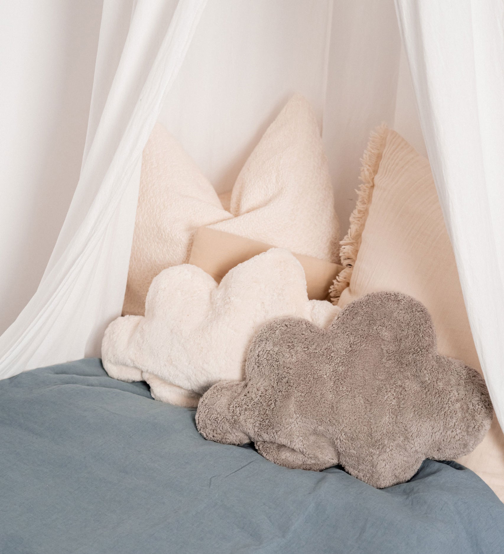 A white and grey cloud shaped Senger warming cushions placed on a bed.
