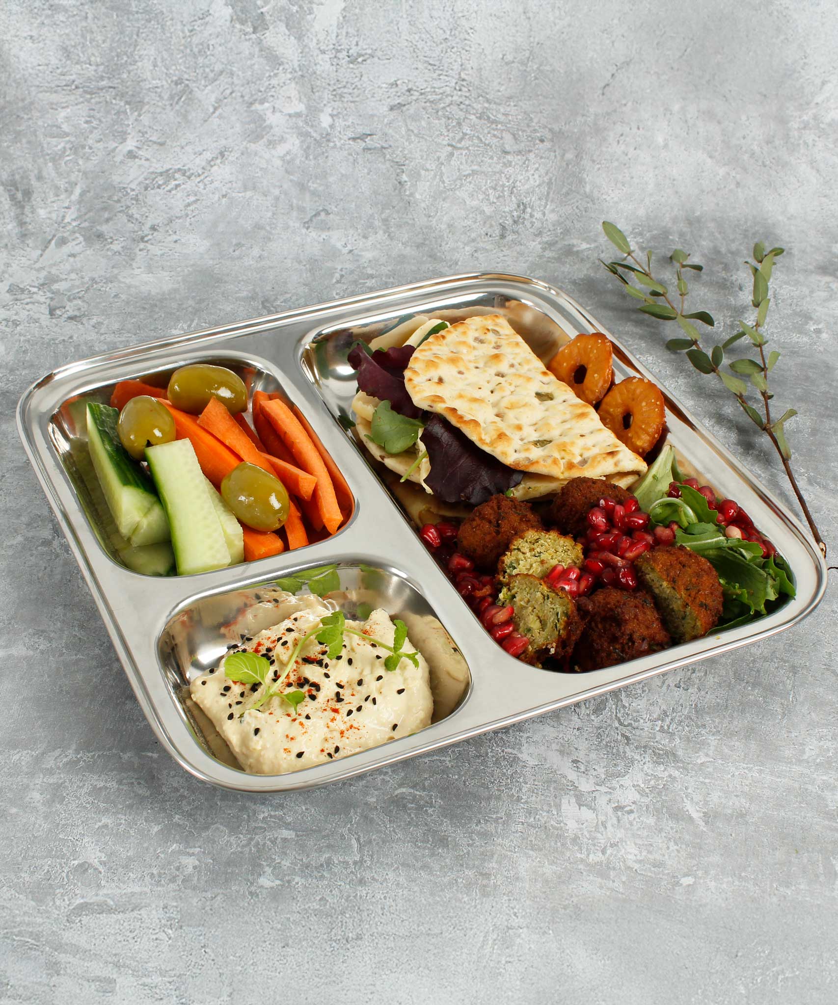 A Slice Of Green Stainless Steel Divided Plate. The plate has hummus in the smallest section, carrot, cucumber and olives in the middle section and flatbread, salad and falafels in the biggest section. This stainless steel plate is suitable for snacks and meals and perfect for children and adults.