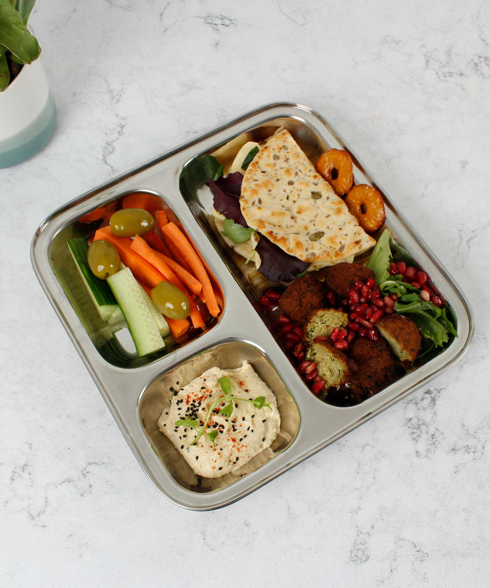 A Slice Of Green Stainless Steel Divided Plate. The plate has hummus in the smallest section, carrot, cucumber and olives in the middle section and flatbread, salad and falafels in the biggest section. This stainless steel plate is suitable for snacks and meals and perfect for children and adults.