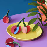 Studio Roof 3D Pop Out Card Cherries. The cherry decorations have been placed on a yellow plate. This 3D pop out card DIY kit is part of Studio Roof's fruits  collection which is available at Babipur.