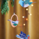 Close up of the Studio Roof plastic-free Calling Birds decorations hanging from a Christmas tree in front of an orange background