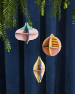 Studio Roof plastic-free hanging Christmas baubles hanging from a Christmas tree in front of a dark blue curtain