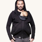 An adult wearing the Love Radius Parent Hoodie in Black, whilst carrying a child inside, on a cream background