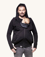 An adult wearing the Love Radius Parent Hoodie in Black, whilst carrying a child inside, on a cream background