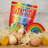 Tonys chocolonely fairtrade mini chocolate easter eggs in the mixed flavours pack on a pile of straw next to a grimms rainbow and some wooden eggs