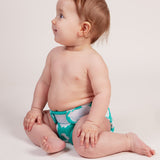 A baby wearing a Tots Bots Bamboozle nappy in the green coloured fluffy clouds print.