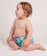 A baby wearing a Tots Bots Bamboozle nappy in the green coloured fluffy clouds print.