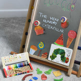 A Triclimb Biri placed on a rainbow Triclimb. A pack of Kitpas crayons have been placed on the floor in front of it. The board has been decorated with hand drawn food illustrations placed under Bajo gruffalo magnets and a caterpillar featured in the very hungry caterpillar book.