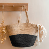 The Turtle Bags hand woven and fair trade jute basket bag with handles, and a black colour block design, hanging on a peg