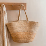 The Turtle Bags hand woven and fair trade jute basket bag with handles, and a natural colour block design, hanging on a peg
