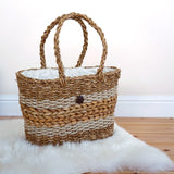 The Turtle Bags hand woven fair trade seagrass basket with handle, positioned on a furry white rug