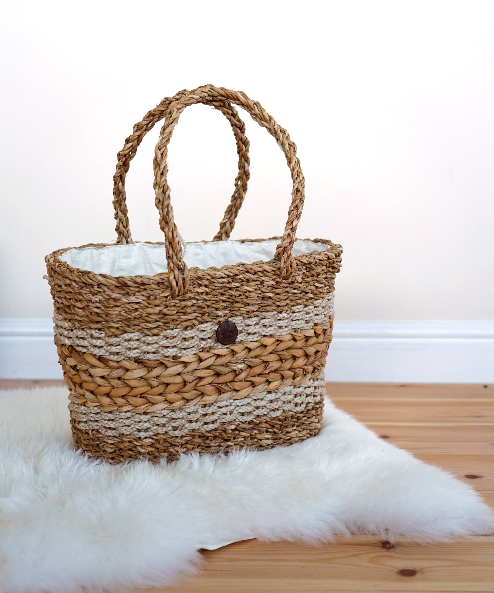 The Turtle Bags hand woven fair trade seagrass basket with handle, positioned on a furry white rug