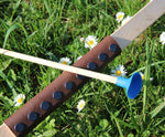 A close up of the brown coloured leather look grip on the Vah Junior Wooden Bow. A blue tipped arrow can be seen alongside it.