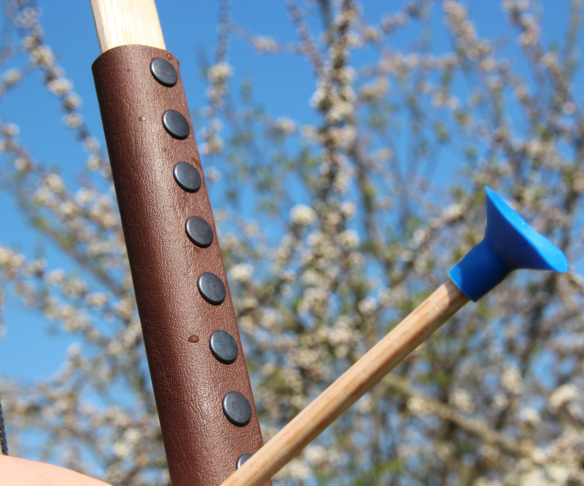 A close up of the brown coloured leather look grip on the Vah Junior Wooden Bow. A blue tipped arrow can be seen alongside it.
