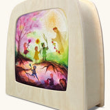 A Toverlux silhouette inside a wooden  lamp. This silhouette has children walking towards a fairy in the spring woods. This layered paper style silhouette is by artist Vogel Geluk and available at Babipur.