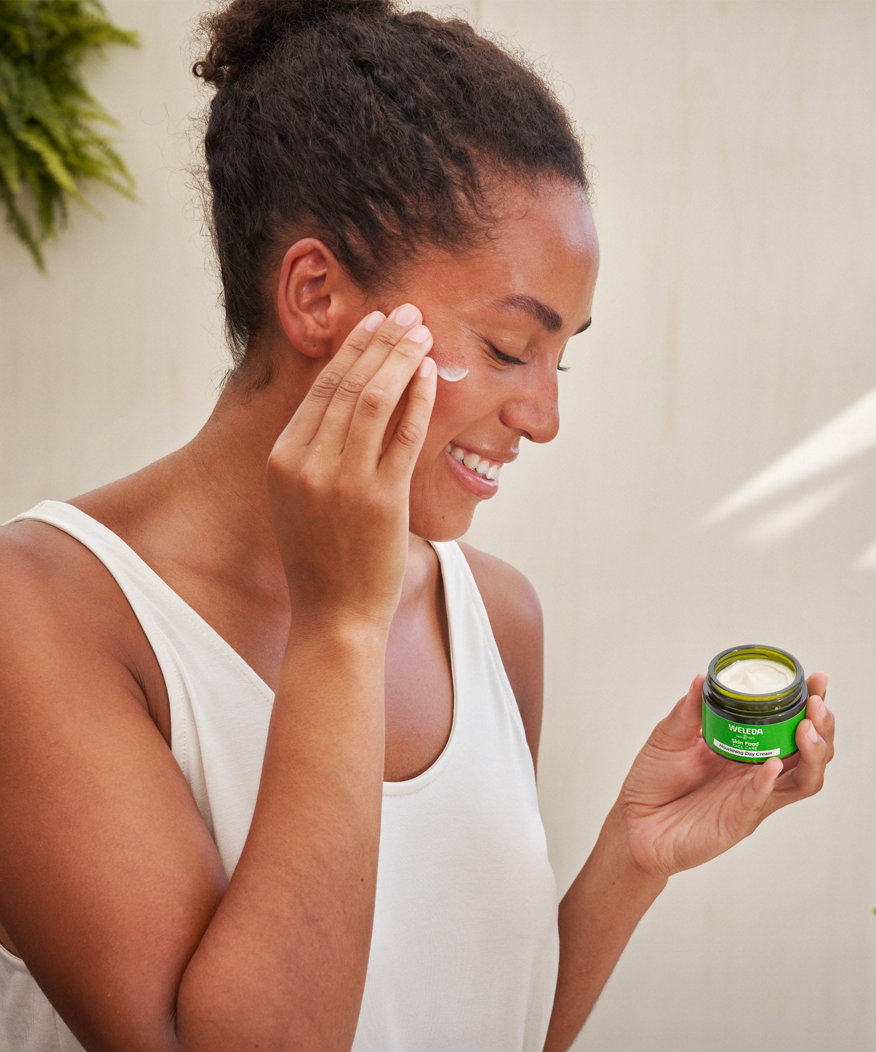 An image of a woman applying the Weleda Skin Food Nourishing Day Face Cream to their cheeks. This cream is available at Babipur.