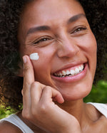 A close up of a woman applying the Weleda Skin Food cream on her cheek. This cream is available at Babipur.