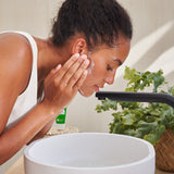 An image of a woman lathering the Weleda Skin Food nourishing cleansing balm above a sink . This cream is available at Babipur.