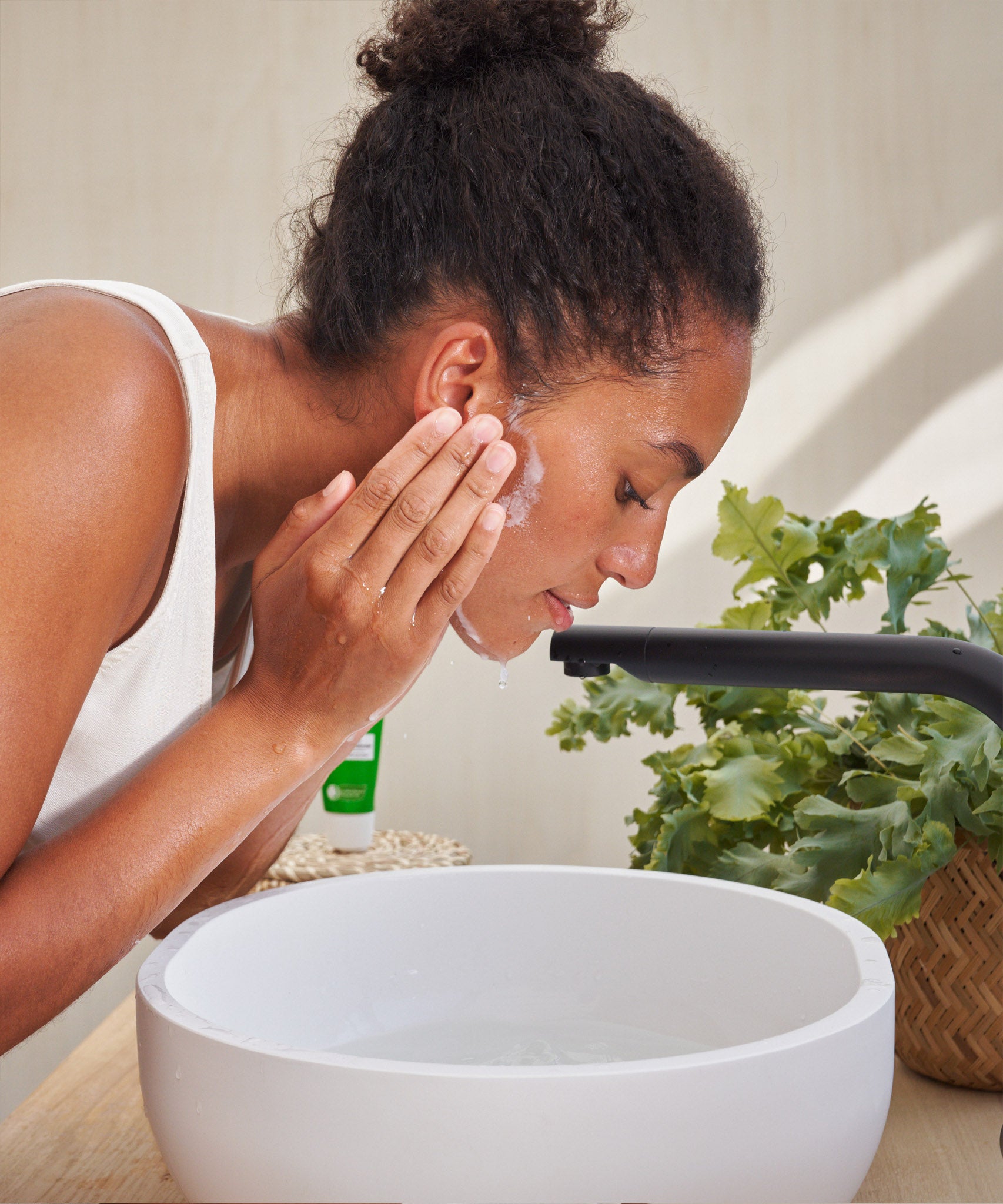 An image of a woman lathering the Weleda Skin Food nourishing cleansing balm above a sink . This cream is available at Babipur.