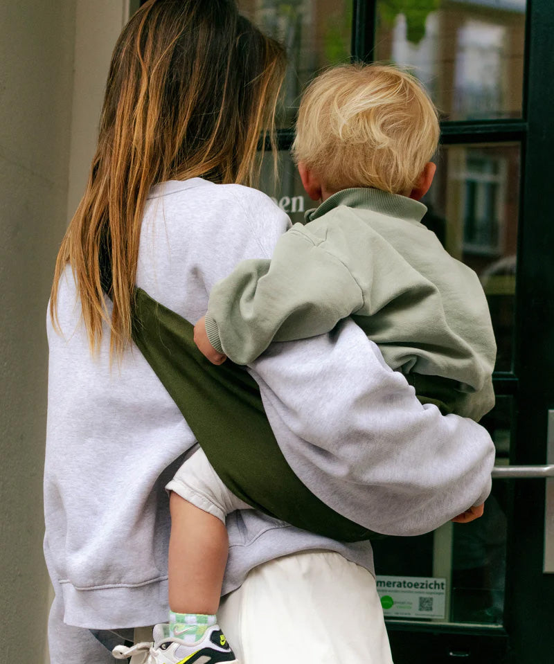 A mother carrying a toddler in the army green Wildride carrier showing the size of the seat and back detail when in use.