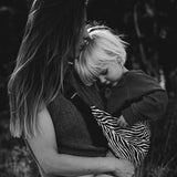 A mother carrying a toddler closely in the black zebra stripe toddler Wildride carrier showing the strap and seat detail