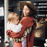 A woman outside a café, carrying her baby in the stylish Wildride hip sling carrier, in a Boho design