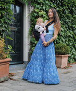 A woman in a long skirt holding her baby with support from the Wildride toddler hip sling carrier, in charcoal grey.