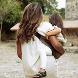 A behind view of a woman carrying her toddler in the coffee brown Wildride hip sling carrier