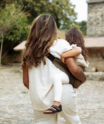 A behind view of a woman carrying her toddler in the coffee brown Wildride hip sling carrier
