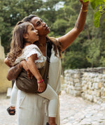 A woman carrying her toddler in the Wildride brown coffee coloured ergonomic hip sling carrier, and admiring nature together
