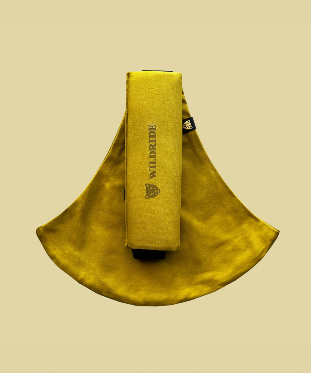 Wildride toddler carrier in desert yellow. A 100% cotton seat stylish hip carrier for babies with brand name on the strap that's folded over the carrier's seat
