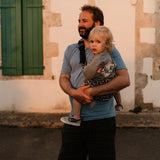 A man carrying his toddler in the special edition 'Feathers' print Wildride hip sling carrier