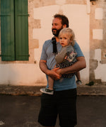 A man carrying his toddler in the special edition 'Feathers' print Wildride hip sling carrier