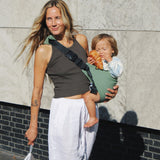 A woman carrying her toddler in the Wildride carrier, in a green fern colour