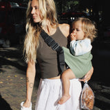 A woman carrying her toddler in the Wildride carrier, in a fern green colour