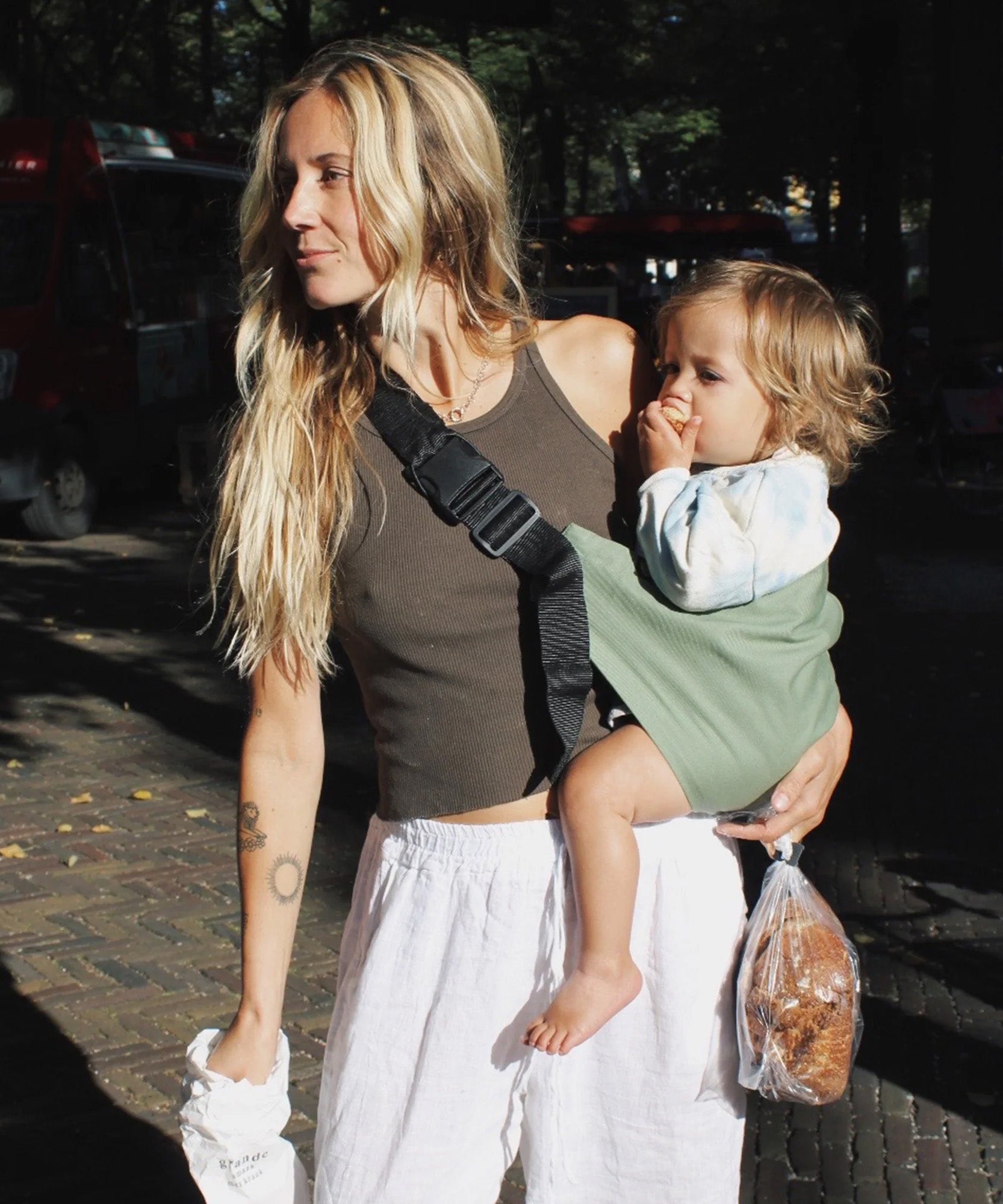 A woman carrying her toddler in the Wildride carrier, in a fern green colour