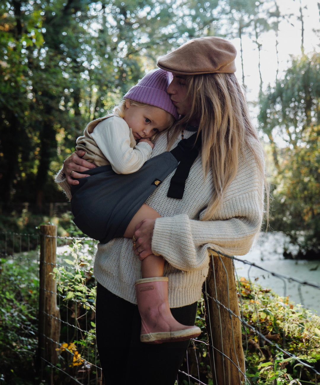A woman and her toddler daughter going on a countryside walk - the daughter is being held in the Wildride ergonomic cotton toddler sling carrier, in an iron grey colour