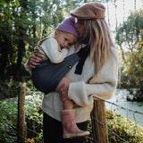 A woman and her toddler daughter going on a countryside walk - the daughter is being held in the Wildride ergonomic cotton toddler sling carrier, in an iron grey colour