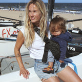 A woman leaning against a yacht, carrying her baby in the stylish Wildride hip sling carrier in grey leopard print