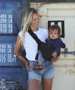 A woman carrying her baby in the stylish Wildride hip sling carrier in grey leopard print